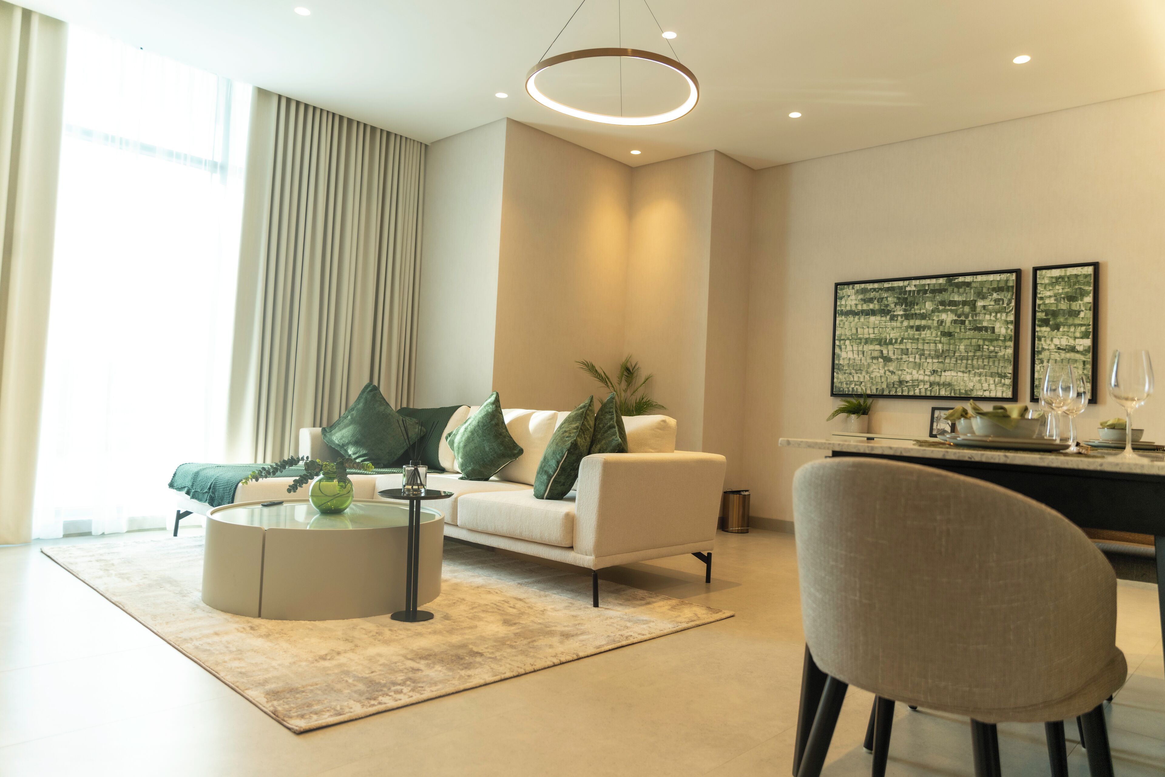 A modern living room with a white sofa, green cushions, a round coffee table, and a dining area with a glass table and chairs.