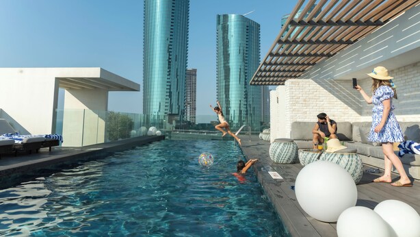 A rooftop pool with clear blue water, surrounded by modern buildings and a wooden pergola. - Pearlhouse Bahrain (Manama)