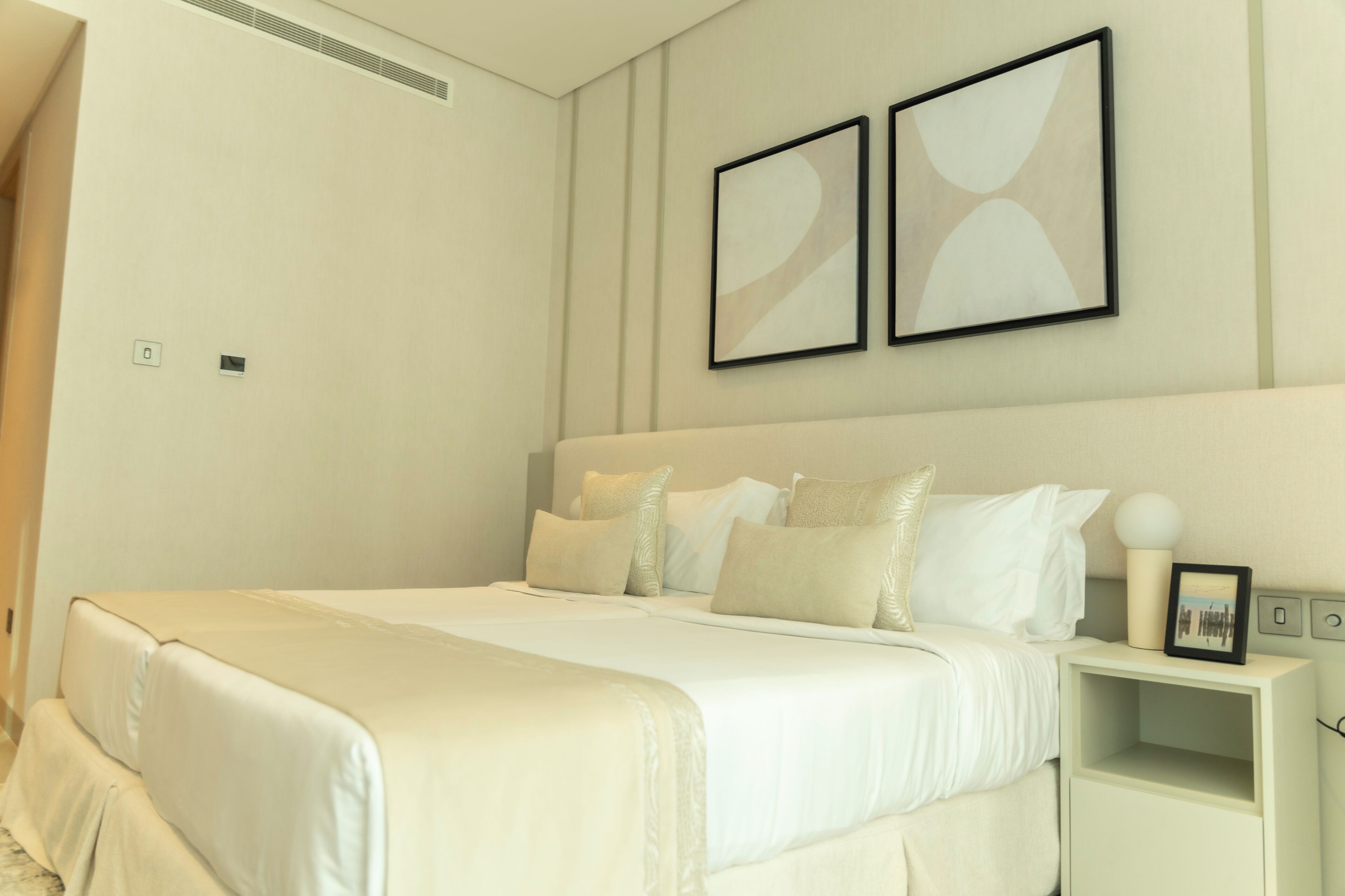 A neatly arranged bedroom with a large bed, a bedside table, and two framed pictures on the wall.