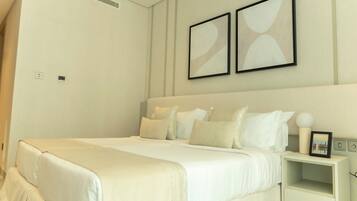 A neatly arranged bedroom with a large bed, a bedside table, and two framed pictures on the wall.