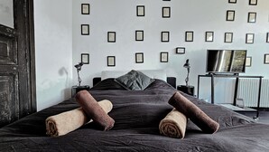 Makuuhuone, jossa on sänky, tyynyjä, televisio ja seinällä kehystettyjä todistuksia.