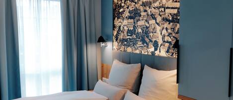 Una habitación de hotel con una cama grande, una mesita de noche, una lámpara y una obra de arte con un paisaje urbano en la pared.