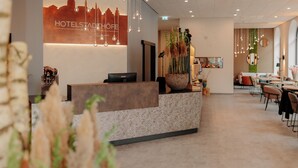 A hotel reception area with a modern design, including a reception desk, seating area, and a wall with a cityscape silhouette. - Stadthöfe Rhede by Hackmann (Rhede)
