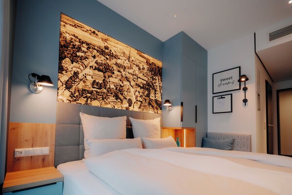 A modern hotel room with a large bed, a headboard with a cityscape mural, bedside lamps, and a wall-mounted artwork with the text "sweet dreams". - Stadthöfe Rhede by Hackmann (Rhede)