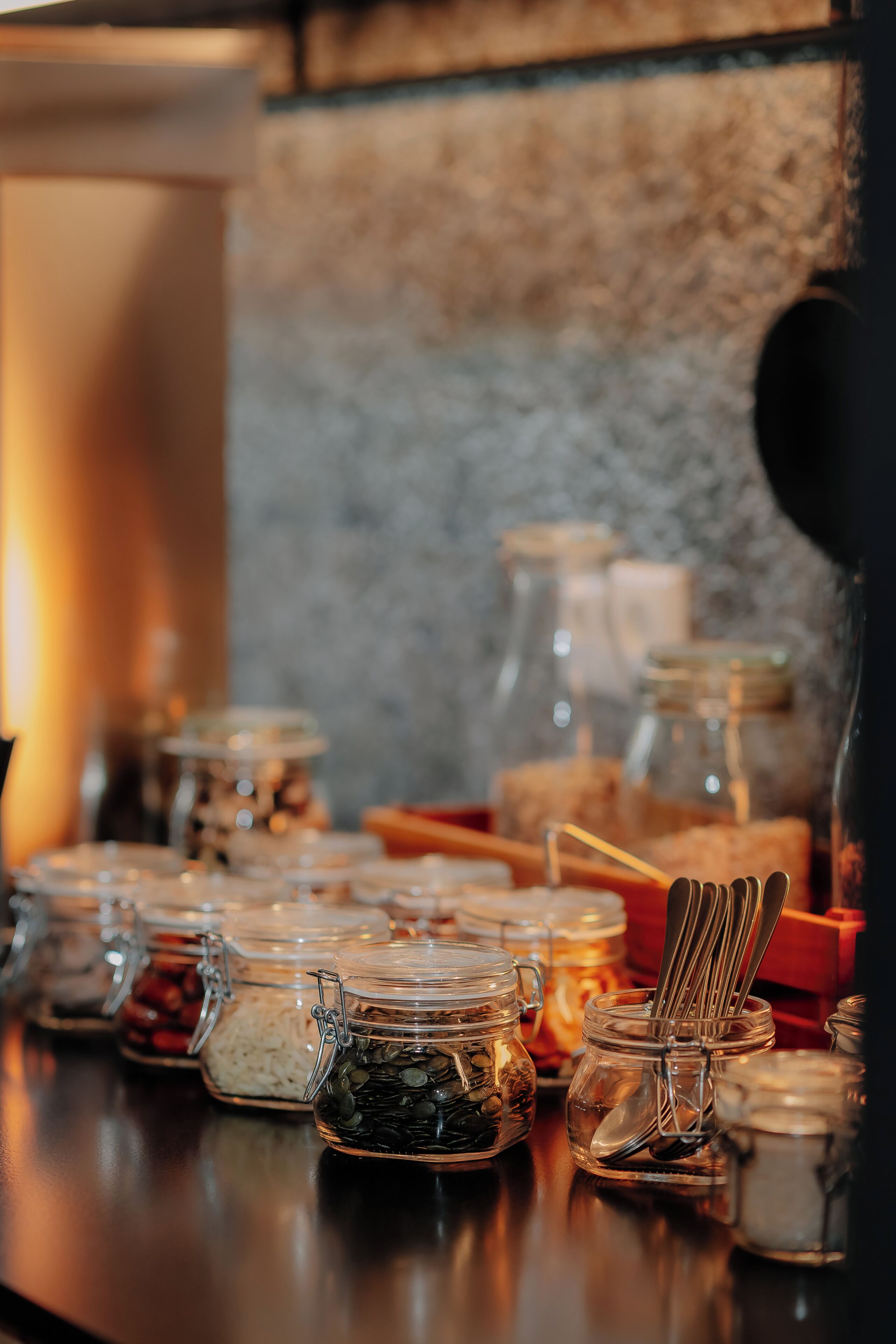 Diversos frascos de vidrio con tapas y asas metálicas, algunos conteniendo distintos tipos de alimentos, sobre una superficie oscura.