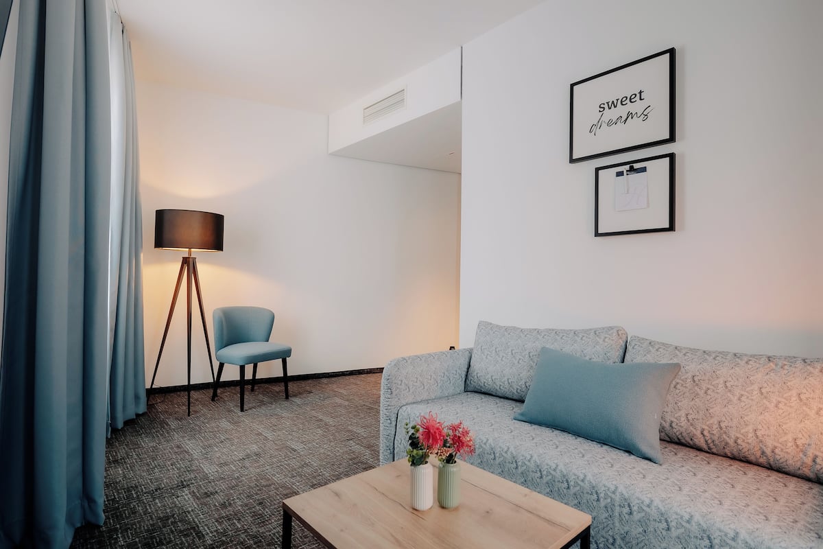 Ein modernes Hotelzimmer mit einer gemusterten Couch, einem kleinen Tisch mit Blumen, einer Lampe und gerahmten Bildern an der Wand.