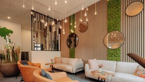 A modern lounge area with sofas, chairs, and a large potted plant. - Stadthöfe Rhede by Hackmann (Rhede)