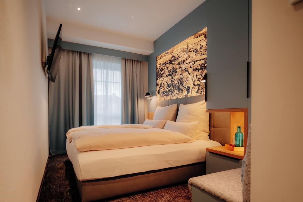 Ein modernes Hotelzimmer mit einem großen Bett, einem Nachttisch mit Lampe, einem an der Wand befestigten Fernseher und einem großen abstrakten Gemälde.