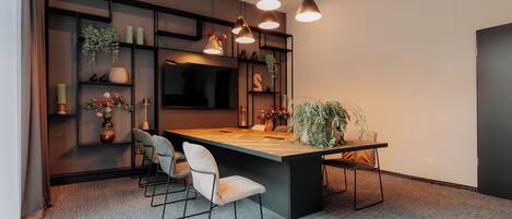 A modern meeting room with a long table, four chairs, and pendant lighting.