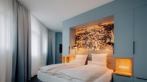 A hotel room with a large bed, a headboard with a cityscape mural, bedside lamps, and a wardrobe. - Stadthöfe Rhede by Hackmann (Rhede)