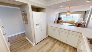 Una cocina moderna con armarios blancos, un refrigerador integrado y un comedor con mesa y sillas de vidrio.