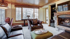 A cozy living room with leather furniture, a fireplace, and large windows overlooking a snowy landscape. - Beautiful Mountain View 2br Condo - Ski-in/out 2 Bedroom Condo (Avon)