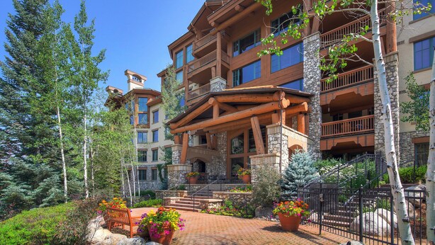 A multi-story hotel with a stone facade, wooden balconies, and a landscaped courtyard with potted plants and a bench. - Beautiful Mountain View 2br Condo - Ski-in/out 2 Bedroom Condo (Avon)