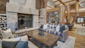 A spacious living area with a stone fireplace, wooden beams, a bookshelf, and a cozy seating arrangement. - Beautiful Mountain View 2br Condo - Ski-in/out 2 Bedroom Condo (Avon)