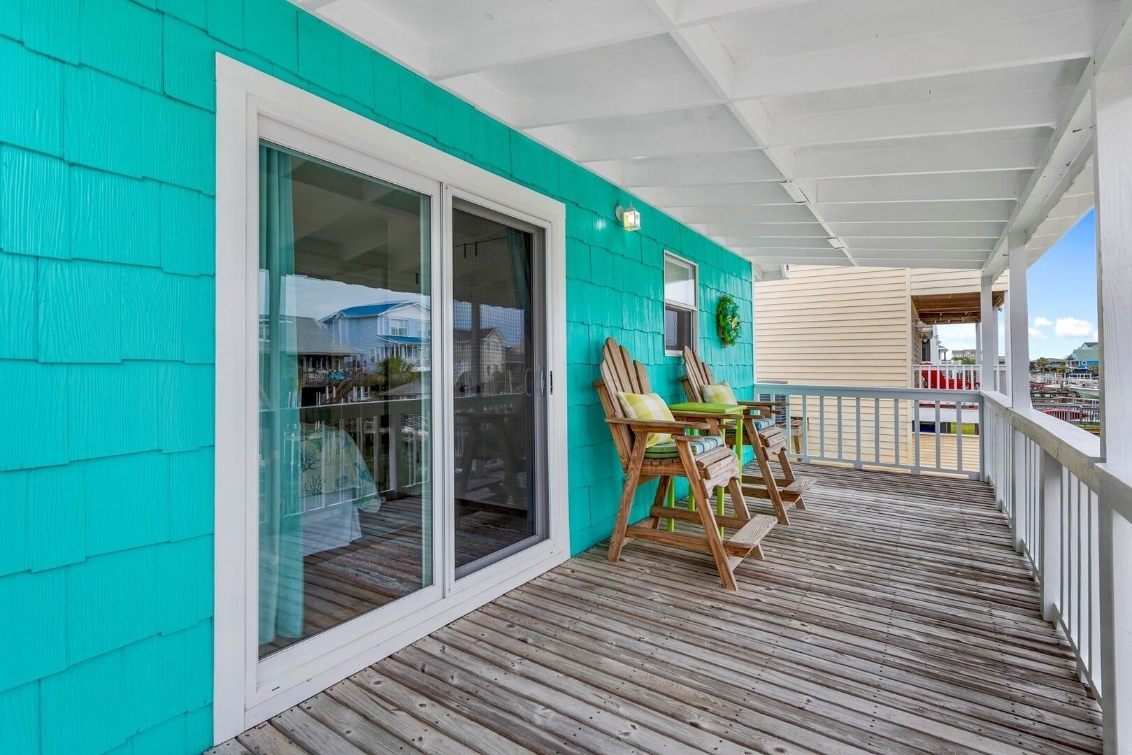 A turquoise exterior wall, a sliding glass door, a wooden deck, and two wooden chairs with cushions.