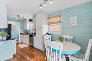 A kitchen with white cabinets, a dining table with white chairs, and a window with blinds.