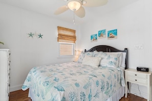 A bedroom with a bed, a nightstand, a ceiling fan, a window with blinds, and wall art. - The Marlin House / 143 Marlin Drive 3 Bedroom Home (Supply)