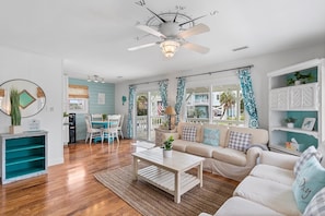 A living room with a ceiling fan, a coffee table, a sofa, and a dining area with chairs. - The Marlin House / 143 Marlin Drive 3 Bedroom Home (Supply)