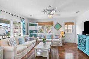 A living room with a sectional sofa, a coffee table, a TV stand, and a ceiling fan. - The Marlin House / 143 Marlin Drive 3 Bedroom Home (Supply)