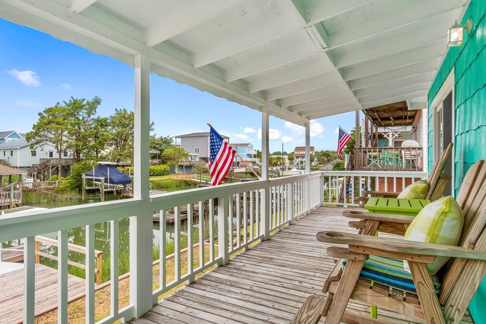 A covered wooden deck with a railing, outdoor furniture, and American flags.