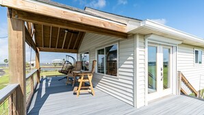 Une terrasse couverte avec une chaise et une table en bois, un bâtiment blanc doté de grandes fenêtres et une vue sur le paysage.