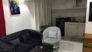 A living room with a black sofa, a grey armchair, and a glass coffee table. There is a kitchen area with a refrigerator, microwave, and sink. - Comfort with elevator: complimentary breakfast buffet  (Dakar)