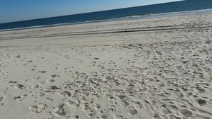 Une plage de sable avec des empreintes et un ciel bleu clair.