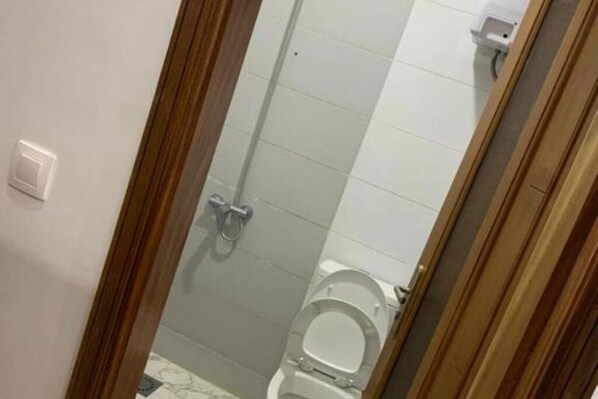 A bathroom with a toilet, a shower, and a hand dryer.