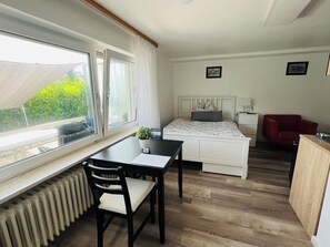 Ein Schlafzimmer mit Bett, Nachttisch, Stuhl und einem Fenster mit Blick auf Grünfläche.