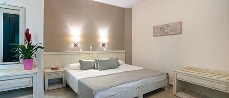 A bedroom with a bed, bedside tables, a nightstand, a potted plant, and a wall-mounted light fixture.