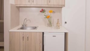 Una cocina compacta con armarios de madera, encimera blanca, un lavabo y un refrigerador pequeño.