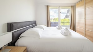 Una habitación de hotel con una cama, una mesita de noche, un ventanal con vistas a la Torre Eiffel y un armario de madera.