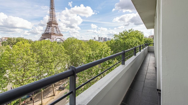 Un balcón con vistas a la Torre Eiffel, árboles y un paisaje urbano.