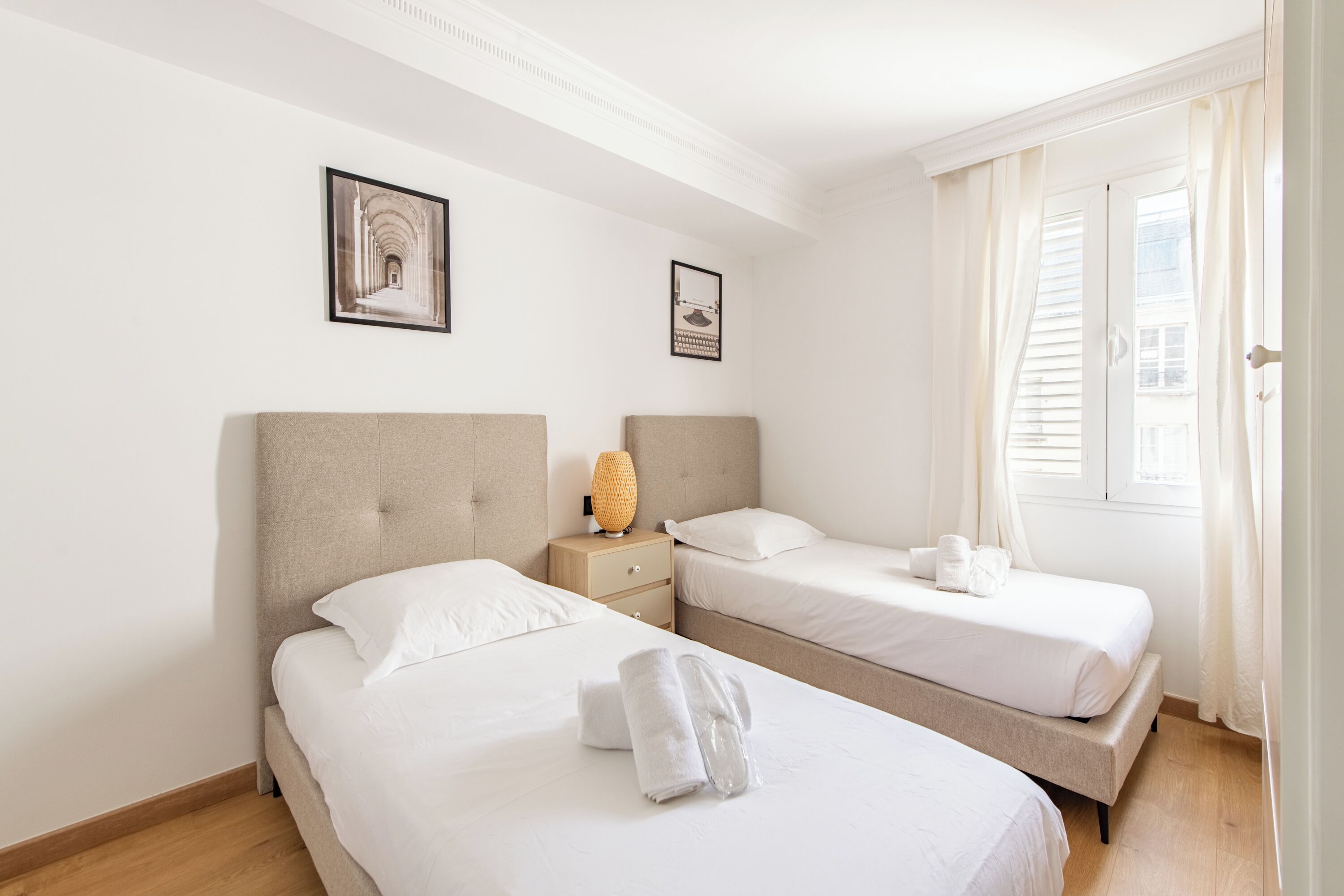 A hotel room with two beds, a nightstand, and a window with curtains.