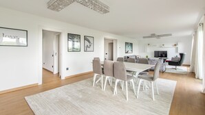 Amplia sala de estar con una mesa de comedor, sillas, un sofá y un televisor. En las paredes hay cuadros enmarcados y un candelabro.