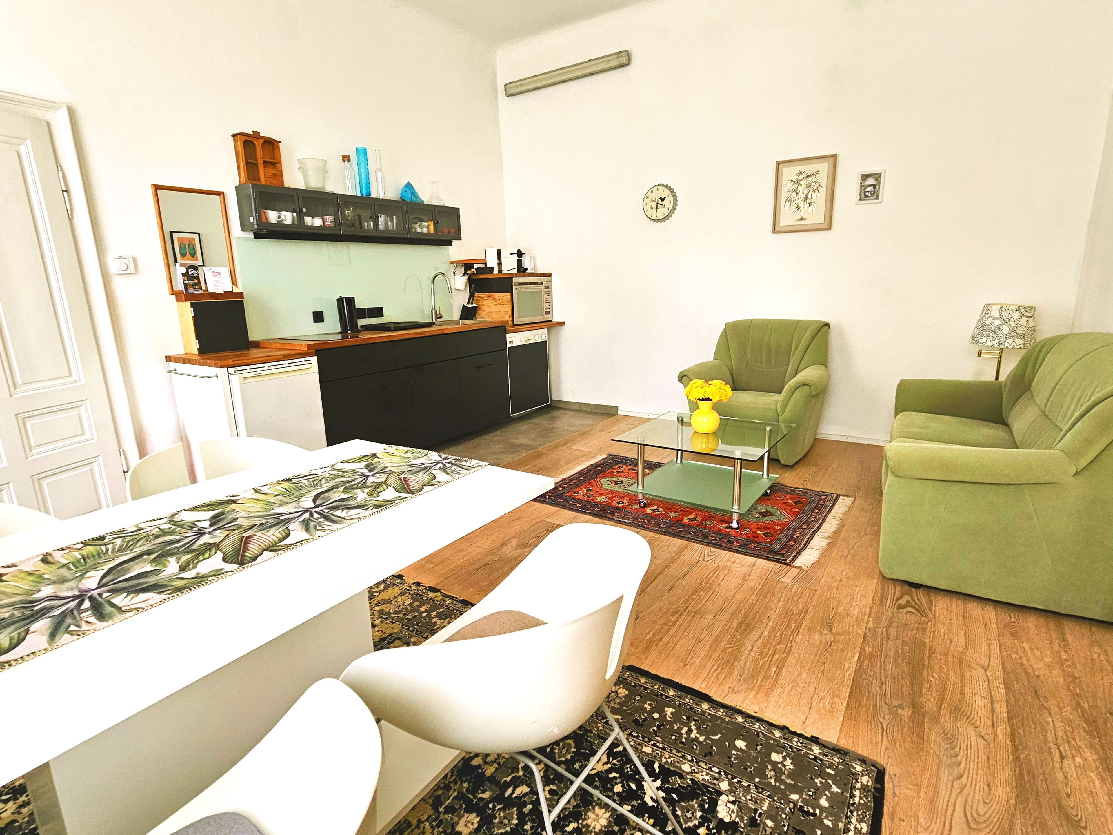 Una sala de estar moderna con comedor, un sillón verde y una cocina al fondo.