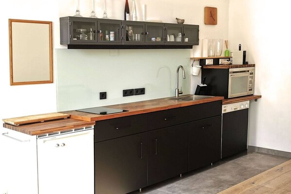 Une cuisine moderne avec un plan de travail en bois, des meubles de couleur noire, un four à micro-ondes encastré et un lave-vaisselle.