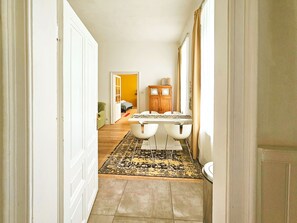 Un couloir mène à une salle à manger où se trouvent une table et des chaises, un buffet en bois et un tapis à motifs.