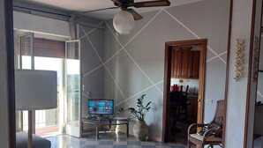 Ein geräumiges Wohnzimmer mit einem großen Fernseher, einem Deckenventilator und einem Schachbrettboden.