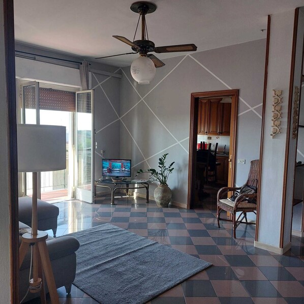 A spacious living room with a large TV, a ceiling fan, and a checkered floor. - Between the Mountains and the Sea (Carrara)