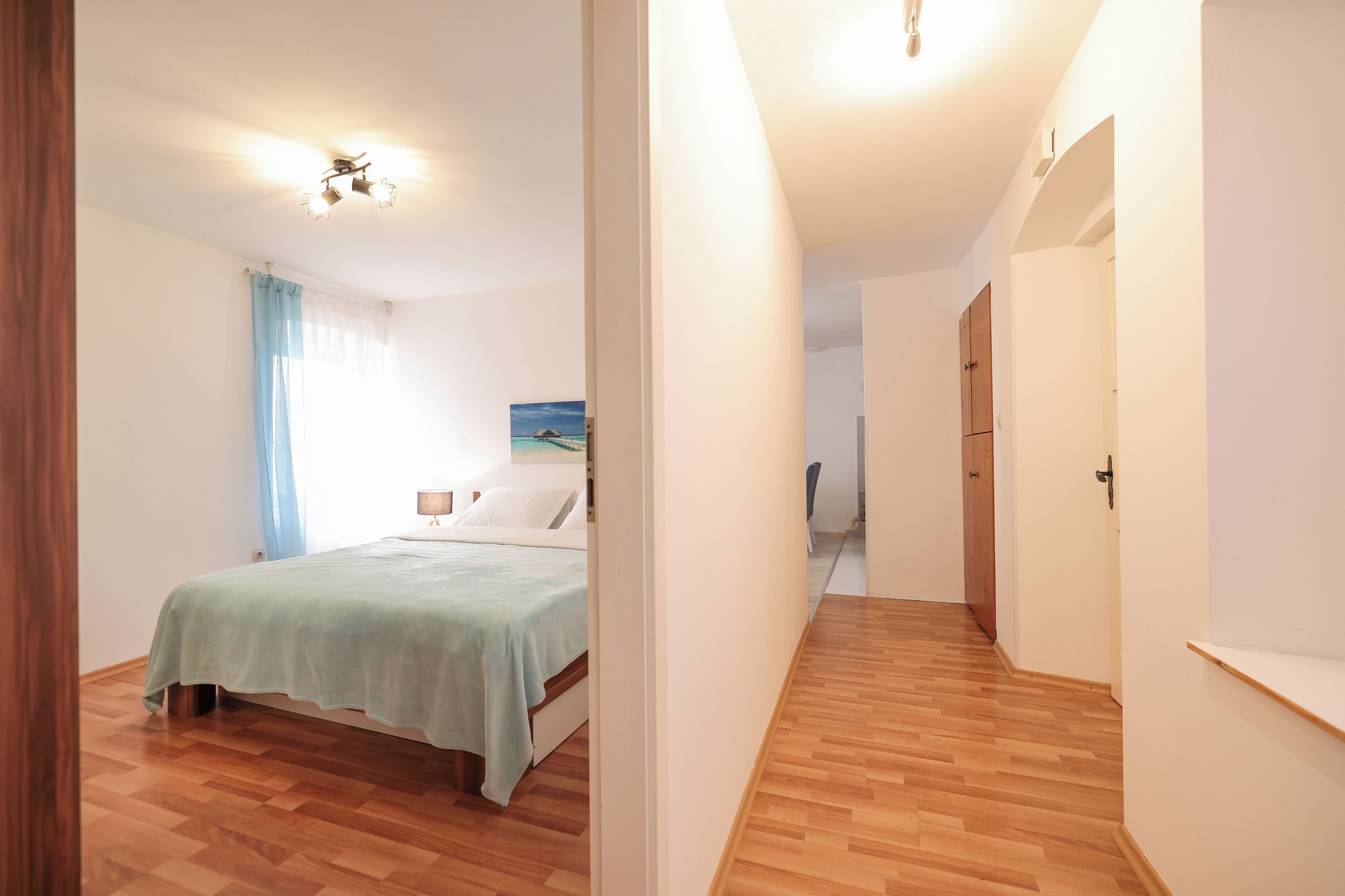 Una camera da letto con un letto, un comodino, una finestra con tende e un quadro appeso al muro.
