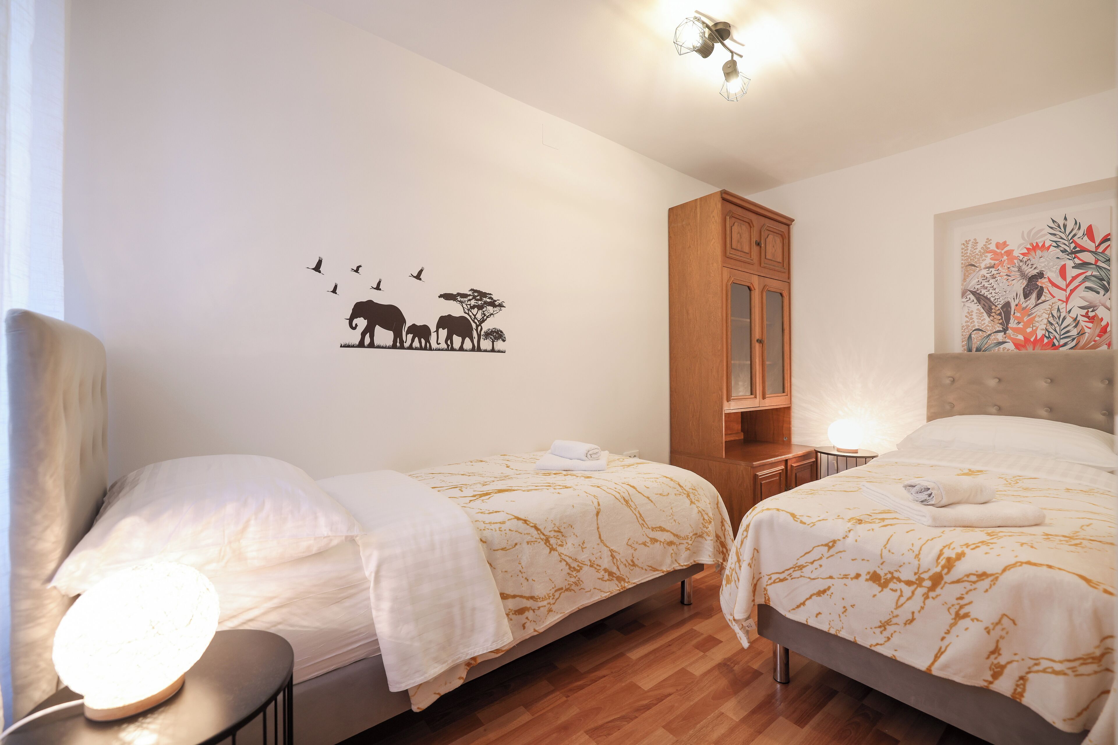 A hotel room with two beds, wooden flooring, a cabinet, and a wall decal of animals.