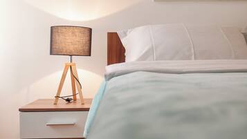A bedroom with a wooden nightstand, a lamp, a bed with white bedding, and a picture of a beach on the wall.