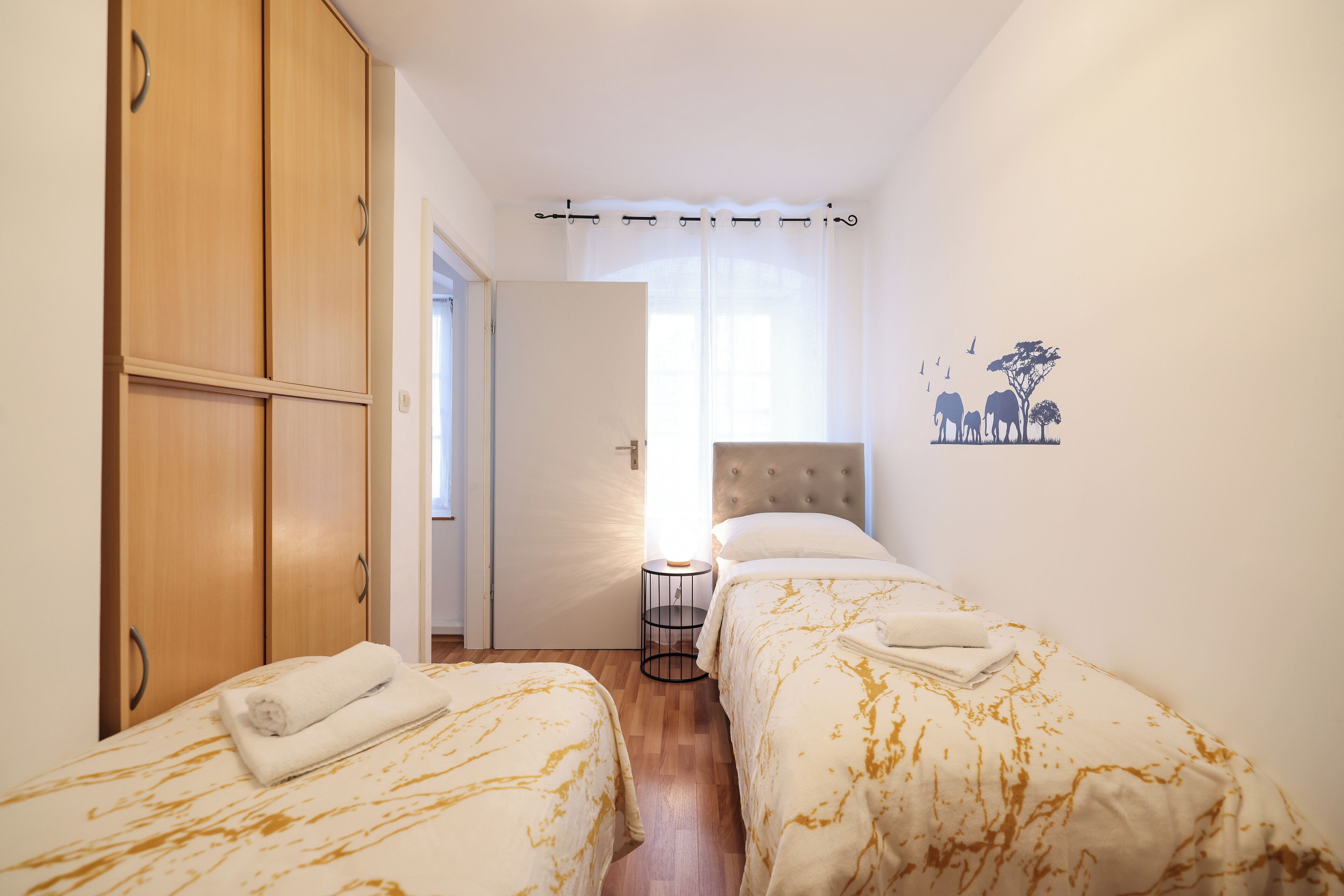 Een slaapkamer met twee bedden, een houten garderobe en een nachtkastje met een lamp.