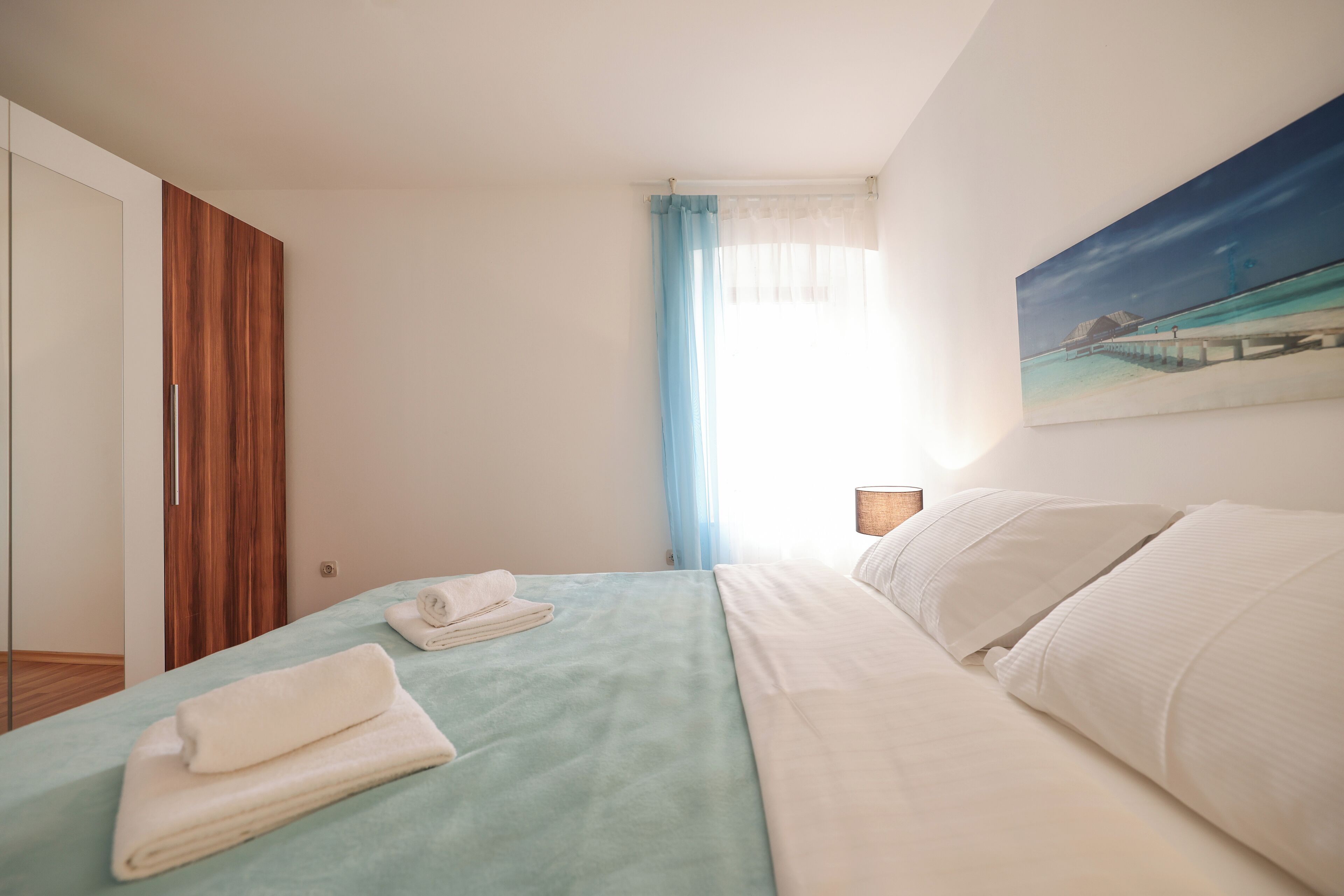Un dormitorio con cama, un cuadro, una ventana con cortinas y un armario de madera.
