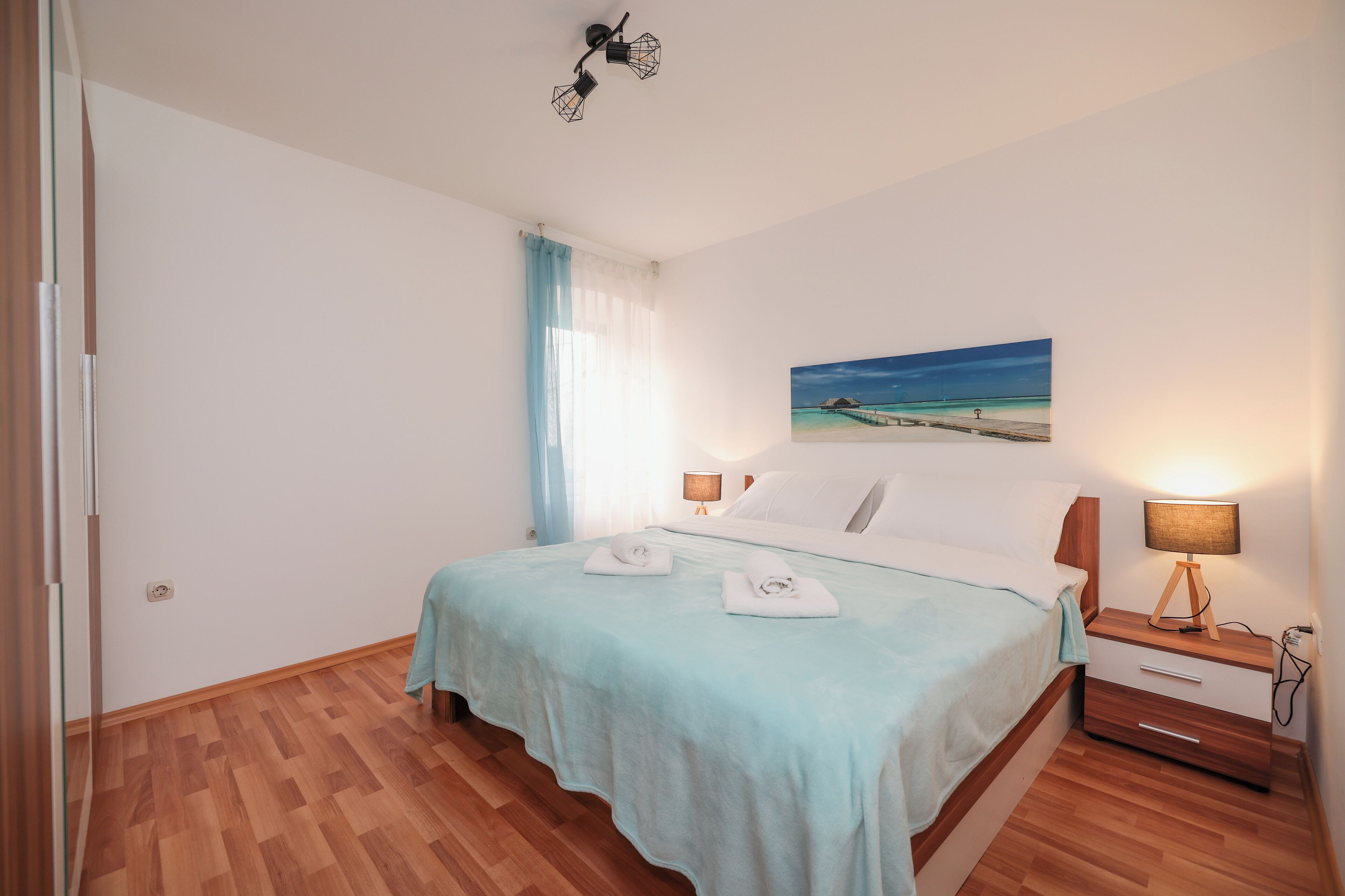 Un dormitorio ordenado con una cama, mesitas de noche, un cuadro y suelo de madera.