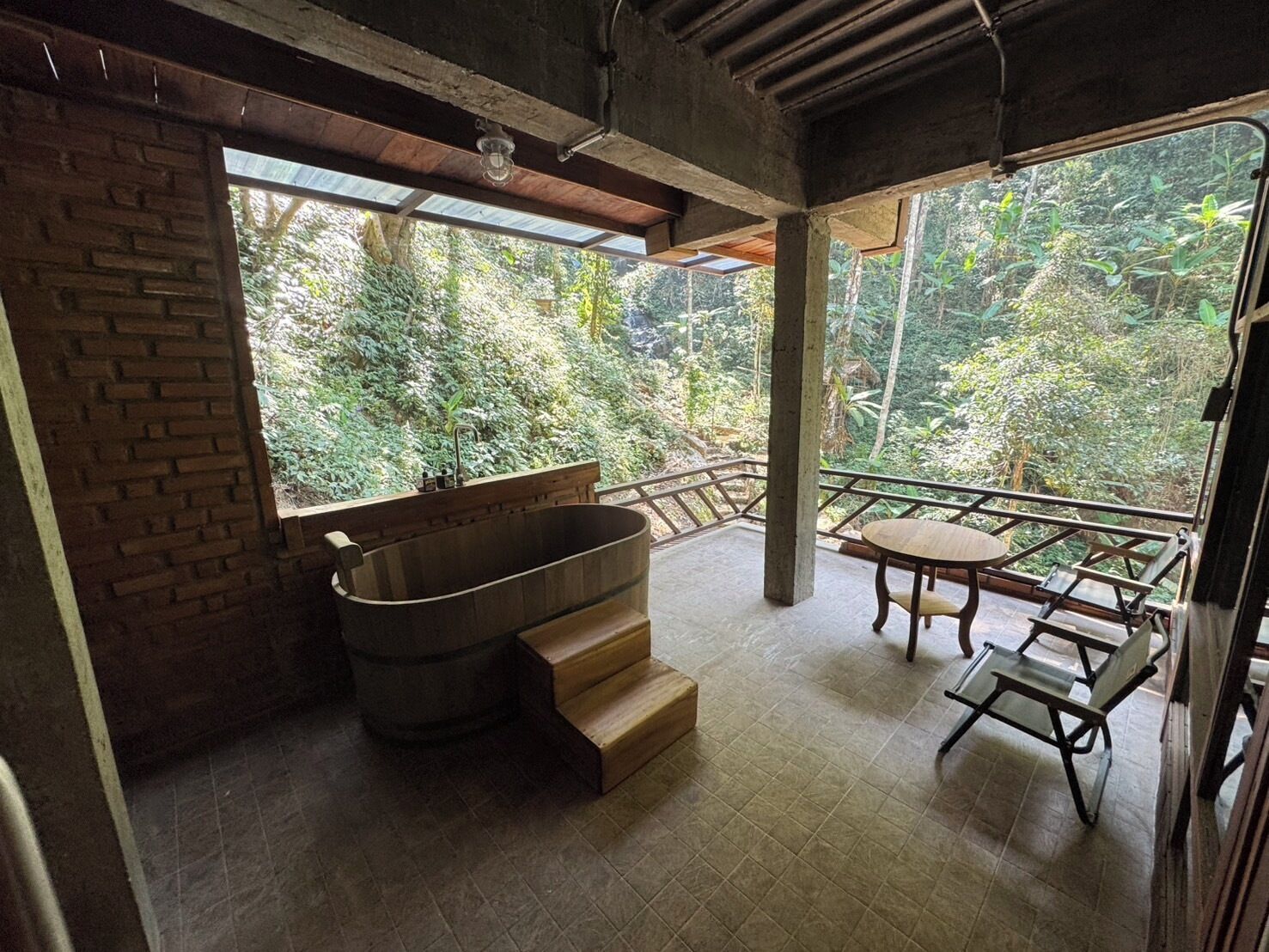 Un baño con una bañera de madera, una mesita pequeña y sillas, y vistas a un jardín exuberante.
