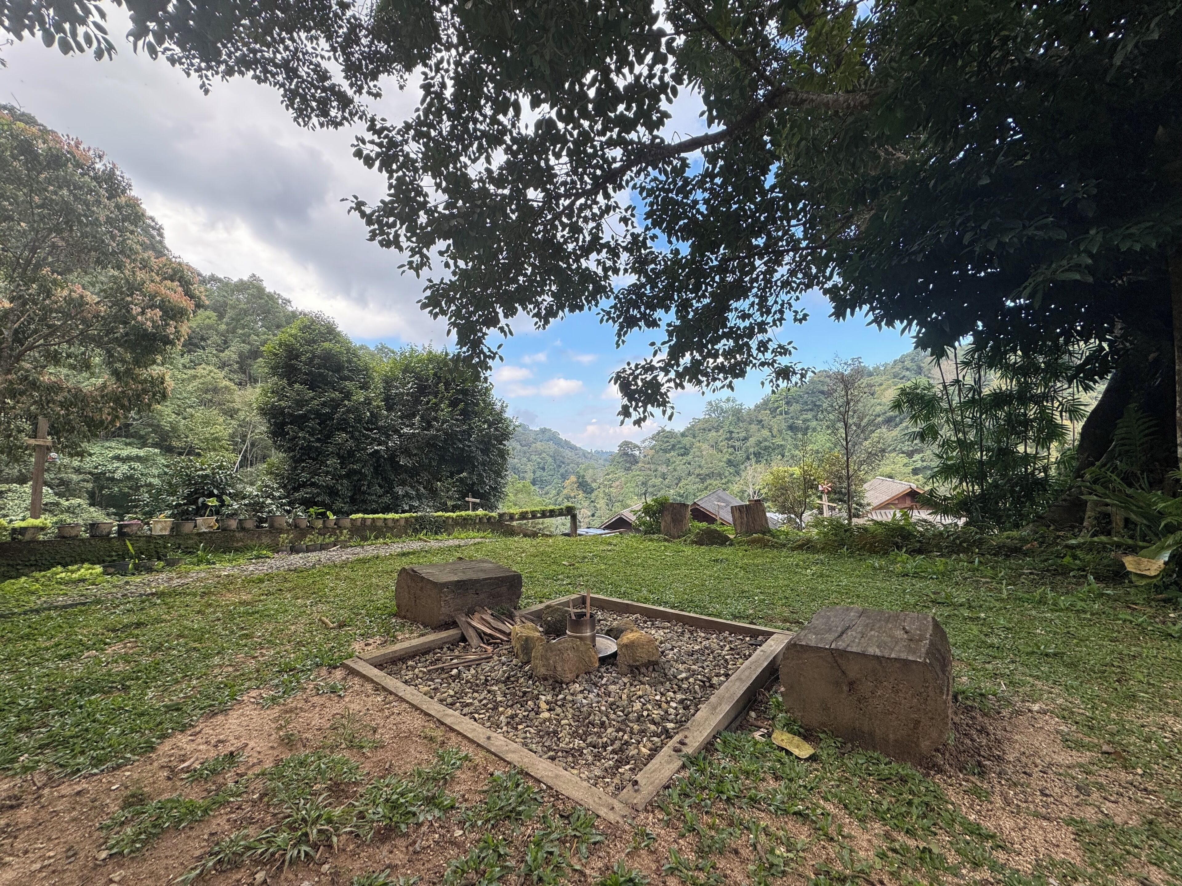 Un jardin paisible avec un foyer, entouré d’une végétation luxuriante et d’un mur de pierre.