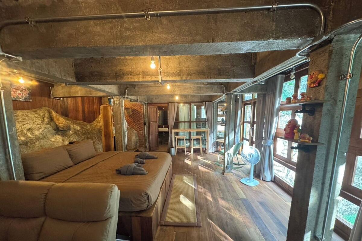 A rustic room with a large bed, wooden walls, and a window with a view of greenery.