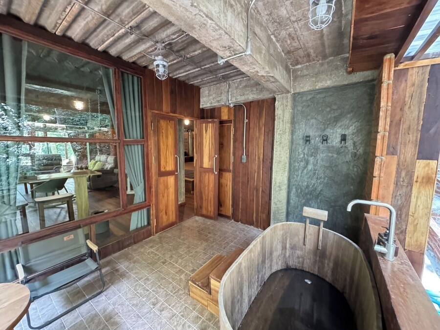 A rustic cabin interior with a large window, wooden walls, a tiled floor, and a wooden bathtub.
